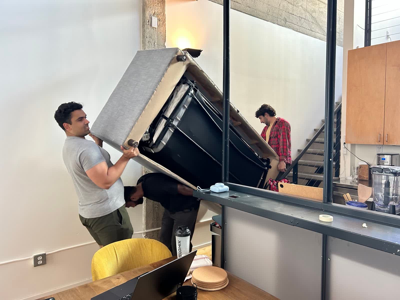 Satya carries a couch into the new office while Avi looks on